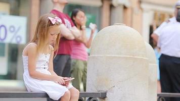 adorable petite fille avec un téléphone intelligent lors d'une journée chaude à l'extérieur dans une ville européenne video
