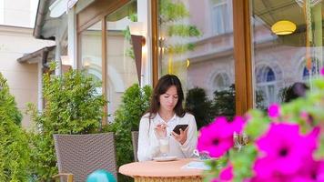 jeune fille avec une tasse de café à l'aide d'un téléphone intelligent prenant selfie au café en plein air. belle femme après la promenade assise dans un café en plein air avec du café et à l'aide d'un smartphone video