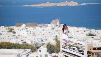 Beautiful young woman relaxing near pool with book in rich hotel with amazing view on Mykonos, Greece