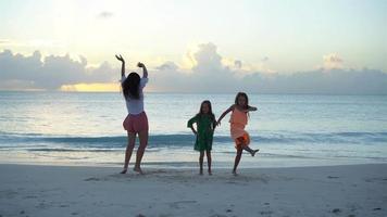 Adorable little girls and young mother having fun on white beach. video