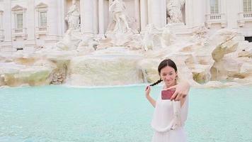 jovem mulher com telefone inteligente tomando selfie ao ar livre na cidade europeia perto da famosa fontana di trevi video