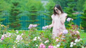 ung flicka i en blomma trädgård bland skön rosor. lukt av ro video