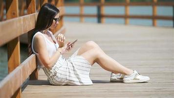 linda mulher está lendo mensagem de texto no celular enquanto está sentado no parque. video