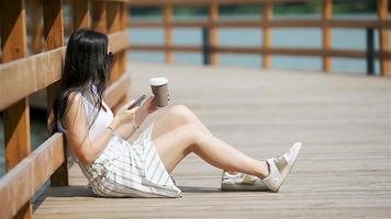 una mujer linda está leyendo un mensaje de texto en el teléfono móvil mientras está sentada en el parque. video