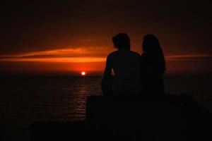 joven pareja enamorada contra la puesta de sol en el mar foto