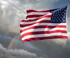bandera americana contra un cielo nublado con un arco iris foto
