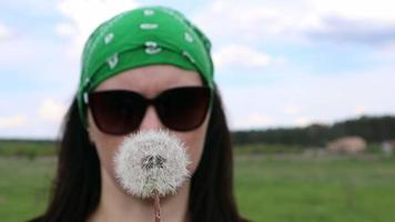 Portrait of a beautiful young woman on a summer lawn, with a ripe dandelion in her hand on a sunny day outdoors. Enjoy nature. Allergy free concept. video