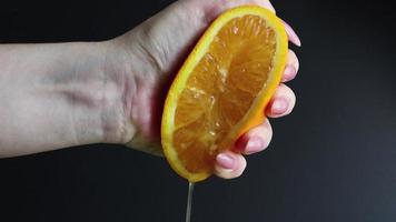 una mano femenina exprime la mitad de una naranja fresca y jugosa. jugo de naranja cítrico goteando de pulpa de naranja sobre un fondo negro. el concepto de dieta saludable, dieta y preparación de una bebida refrescante. video