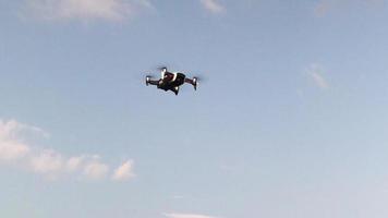 A drone hovering at low altitude with a camera photographing aerial views against the backdrop of a cloudy sky. The quadcopter hangs in the air, bottom view. Fast rotating drone propellers video