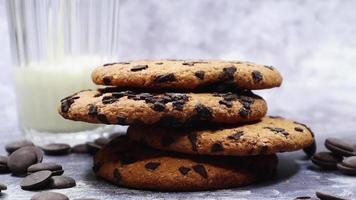 American chocolate chip cookies, milk is poured into a glass in the background on a gray background. Traditional round crispy dough with chocolate chips. Bakery. Delicious dessert, pastries. video