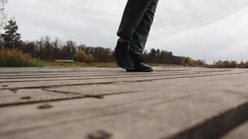 A woman walking in boots, jeans and a jacket on a wooden bridge over a lake in autumn weather, a cheerful happy journey without worries. Relaxation, enjoying life in nature, low viewing angle. video