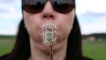 porträtt av en skön ung kvinna på en sommar gräsmatta blåser på en mogen maskros på en solig dag utomhus. njut av natur. allergi fri begrepp. video