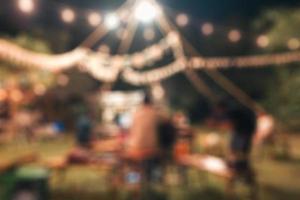 Blurred scene of group of friends with BBQ picnic party and illuminated campfire in backyard photo