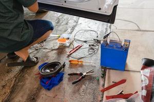 Mechanic man fixing the car with speaker equipment, pliers, wire and battery in workplace photo