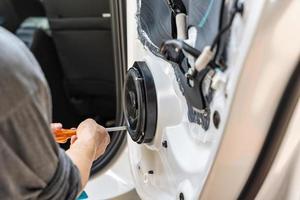 Mechanic using screwdriver screwing drywall screw with car speaker on vehicle door photo
