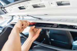 Hand of mechanic using wedge removing and installing a dash cam inside a car at workshop photo