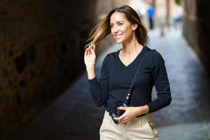 señora confiada con cámara sonriendo y tocando el cabello en la calle foto