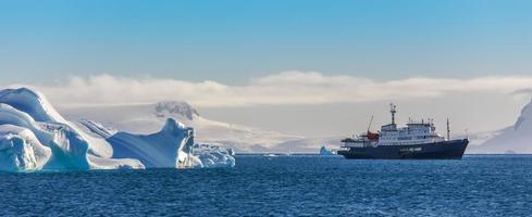 barco de crucero azul entre los icebergs con glaciar en el fondo, islas shetland del sur, antártida foto