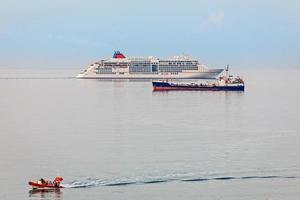 Passenger cruise liner, cargo ship and small boat in front, on t photo
