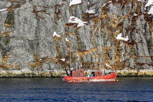 Lone fishing boat floating near steep cliff, Nuuk fjord, Greenland photo