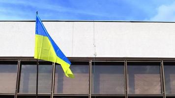 avvicinamento di il nazionale bandiera di Ucraina contro il sfondo di un amministrativo edificio svolazzanti nel il vento. patriottico blu e giallo nazionale bandiera su un' pennone su il costruzione. video