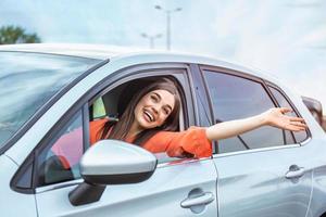 mujer joven sentada en un coche con la mano fuera de la ventana. mujer feliz conduciendo un coche y sonriendo. retrato de una feliz conductora conduciendo un coche con cinturón de seguridad. Linda señorita feliz conduciendo coche. foto