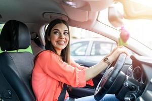 Cute young lady happy driving car. Image of beautiful young woman driving a car and smiling. Portrait of happy female driver steering car with safety belt on photo