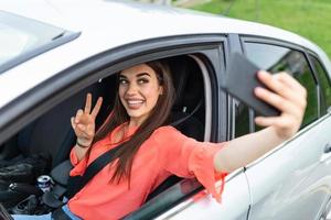 Smiling young woman taking selfie picture with smart phone camera outdoors in car. Holidays and tourism concept - smiling teenage girl taking selfie picture with smartphone camera outdoors in car photo