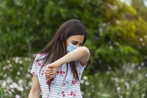 How to sneeze correctly. Woman with protective mask sneezes on the elbow. Concept of not spread of the virus. photo