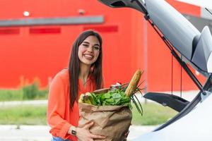 Woman after shopping in a mall or shopping centre and driving home now with her car outdoor. Beautiful young woman shopping in a grocery store supermarket photo