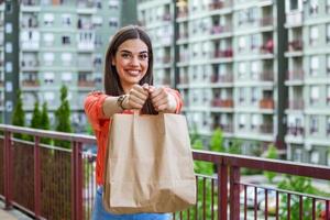 Woman delivering food in paper bag.Female volunteer holding groceries in the house porch. Delivery food service at home. Courier delivered the order no name bag with food. photo