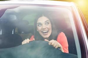 Happy brunette woman driving a car. Portrait of beautiful caucasian woman with toothy smile and brown hair driving car. Hand on steering wheel. Young woman driving a car in the city photo