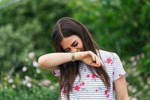 joven mujer bonita estornudando frente a un árbol floreciente. concepto de alergia primaveral. alergias estacionales y problemas de salud. dolor de senos paranasales que causa dolor de cabeza muy doloroso. síntoma de resfriado de gripe. dolor de sinusitis foto