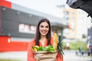 mujer después de comprar en un centro comercial o centro comercial y conducir a casa ahora con su auto al aire libre. bella joven comprando en un supermercado foto