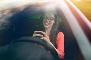 Texting and driving, behind the wheel. Breaking the law. Woman driving car distracted by her mobile phone. Woman typing message on the phone while waiting in the car. photo