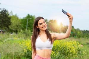 Girl taking a selfie in front of an amazing landscape. Sport woman smile at camera self picture at street, young girl picture herself exercising fitness photo