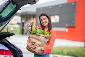 Woman putting her shooping bags into car at shopping mall parking lot. She has done some light shopping,mainly food. Young happy beautiful woman shifts the purchase from shopping cart photo