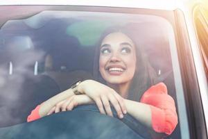 mujer morena feliz conduciendo un coche. retrato de una hermosa mujer caucásica con una sonrisa dentuda y un coche de conducción de cabello castaño. mano en el volante. mujer joven conduciendo un coche en la ciudad foto