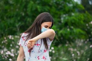 Cómo estornudar correctamente. mujer con máscara protectora estornuda en el codo. concepto de no propagación del virus. foto