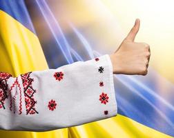 woman in Ukrainian clothes shows symbol ok against Ukrainian flag photo