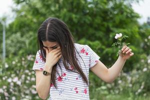 Young woman with Pollen allergy holding a flower and saying no.. Young woman with pollen and grass allergies. Flowering trees in background. Spring Seasonal allergies and health problems. photo