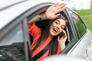 Young woman talking on the phone in the car and waving. Close up portrait of young business woman sitting in the car and laughing while talking on mobile phone photo