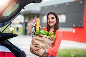 Close up portrait of a happy pretty girl holding bag with groceries and looking at camera with copy space. Close up of a woman holding heavy bag with groceries. Carrying a healthy bag photo