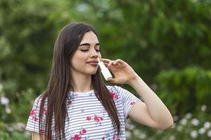 Pollen allergy concept. Young woman using nose spray for her pollen and grass allergies. Flowering trees in background. Spring Seasonal allergies and health problems. photo