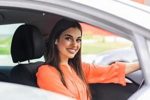 Young Woman Embracing Her New Car. Excited young woman and her new car indoors. Young and cheerful woman enjoying new car hugging steering wheel sitting inside photo