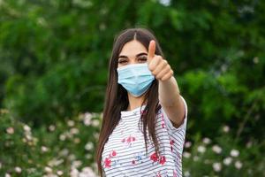 Portrait of young woman wearing face protective mask to prevent Coronavirus and anti-smog. Portrait of young woman wearing face mask. Thumb up photo