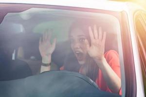Angry young sitting woman pissed off by drivers in front of her and gesturing with hands. Road rage traffic jam concept. Woman is driving her car very aggressive and gives gesture with his fist photo