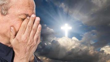 Cross and elderly man with a face closed by hands photo