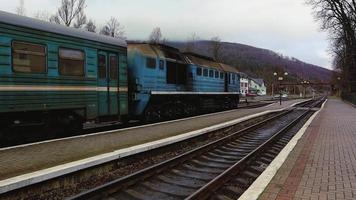 the railway station, a train passes by, in the background mountains. Passengers leave the train on the platform of a small station in a sparsely populated city. Ukraine, Yaremche - November 20, 2019. video