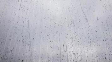 detailopname van water druppels Aan glas. gedurende de herfst regenen, groot druppels vallen Aan de venster deelvenster en stromen naar beneden tegen de lucht in de dag. herfst en regenachtig seizoen concept. slecht het weer. video